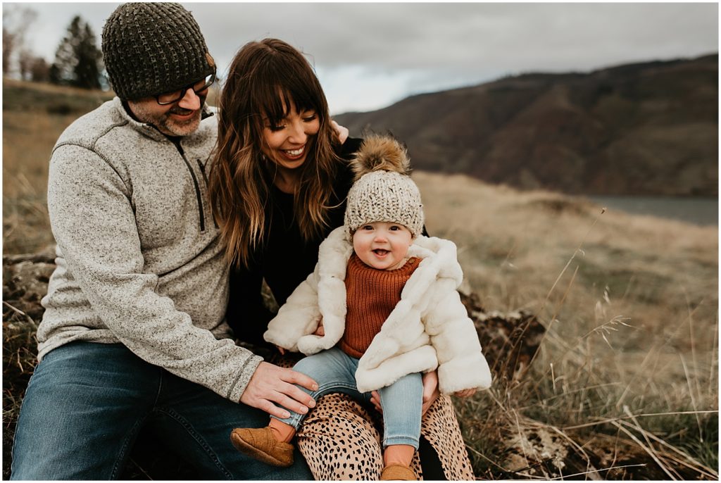 mom and dad sitting on rock with baby in knit hat