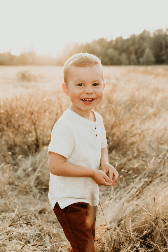 toddler boy smiling at camera in a field
