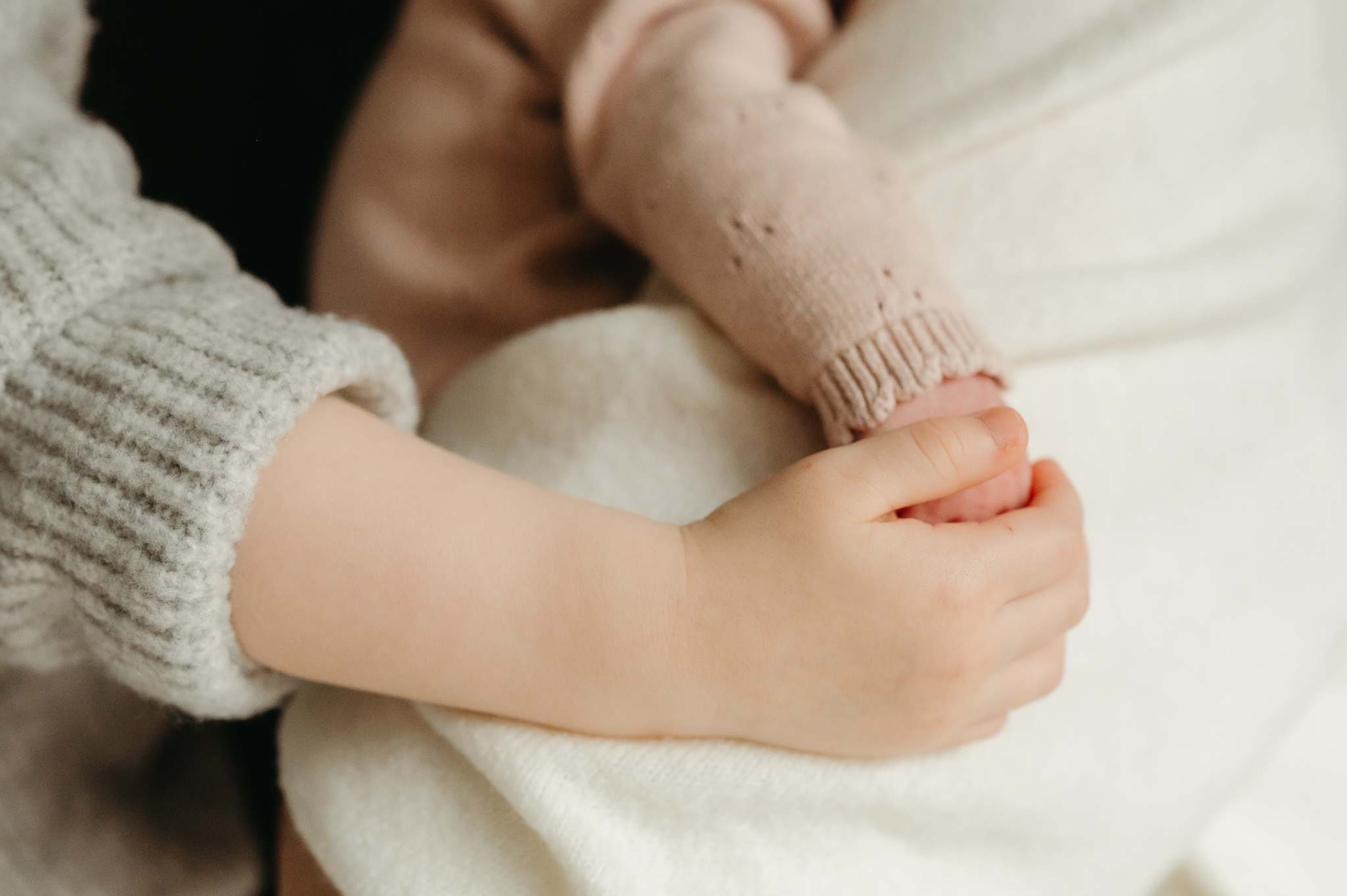 Close-up in-home newborn photography shot of a baby's tiny hands, highlighting precious details in a relaxed and intimate setting.