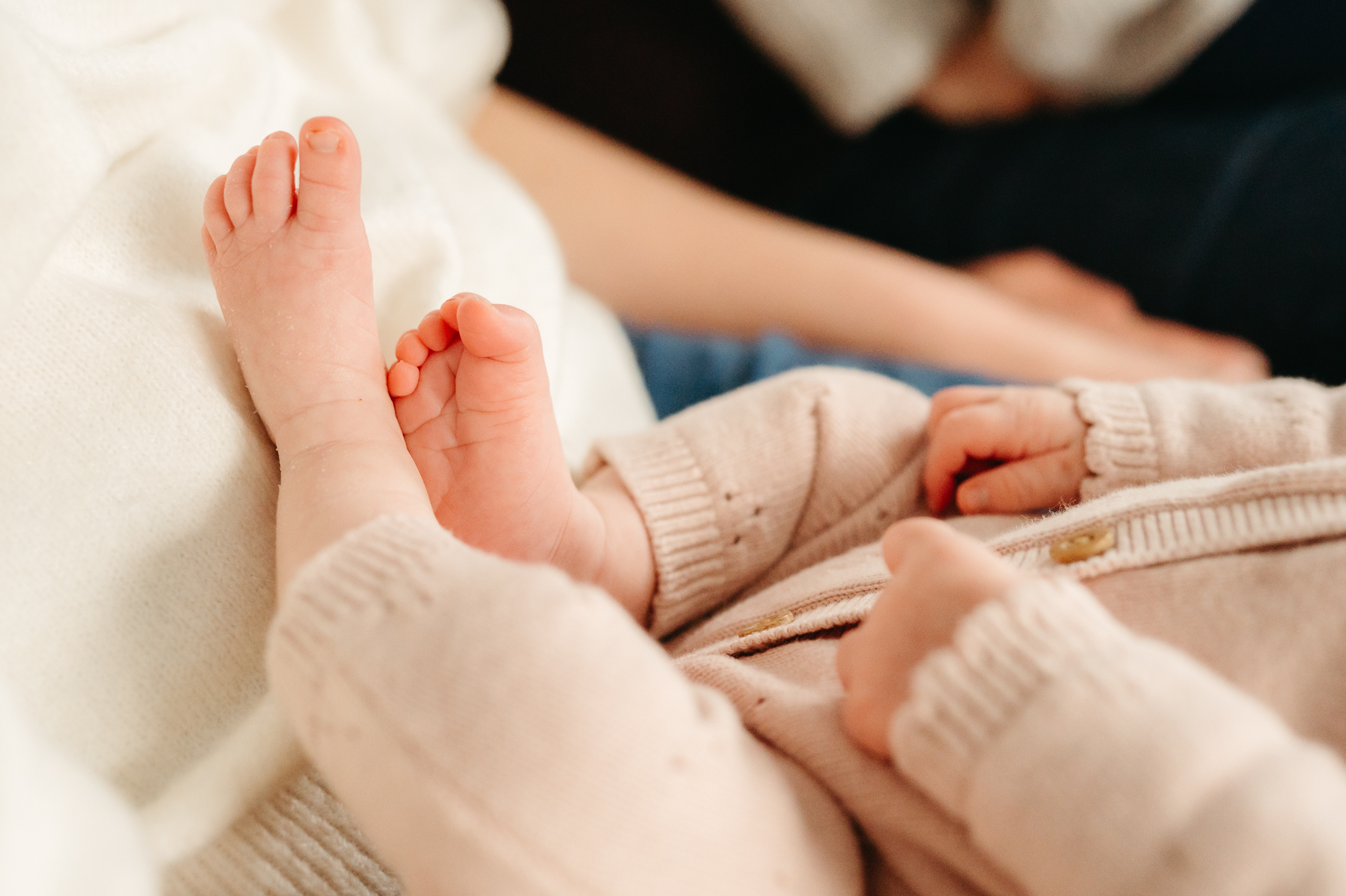 Close-up in-home newborn photography shot of a baby's tiny hands and toes, highlighting precious details in a relaxed and intimate setting.