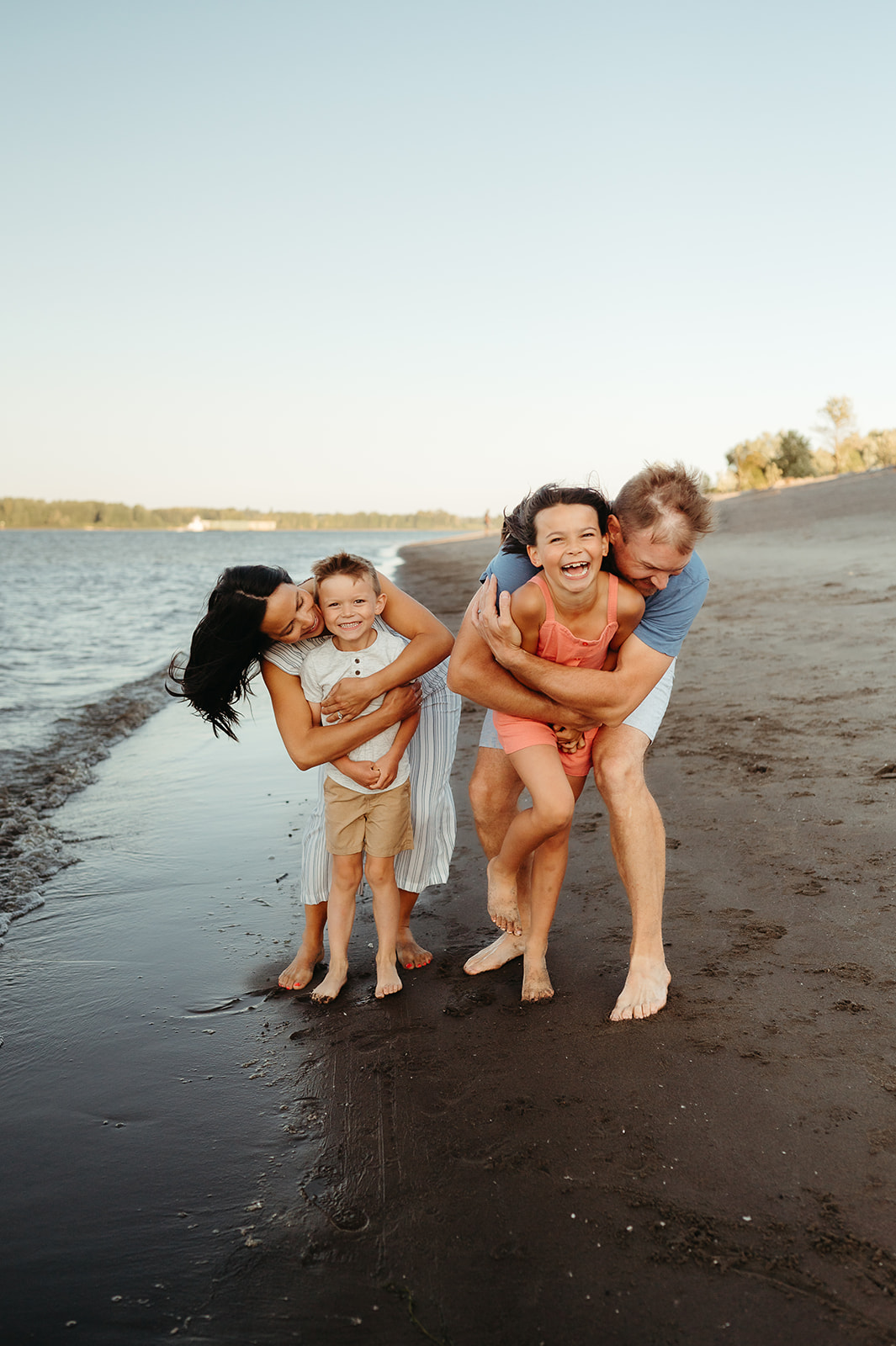 Parents playing and laughing with their children on the shoreline during a sunset family photo session. Barefoot in the sand, this fun and relaxed session captures genuine joy and movement.