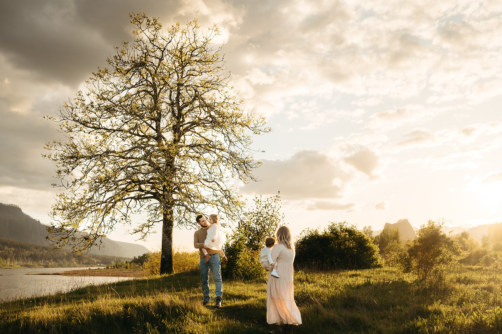 Family of four enjoying a golden hour moment in a scenic Oregon landscape. Parents and children dressed in soft, neutral tones, with a dramatic sky and glowing sunset adding warmth to this timeless outdoor family session.