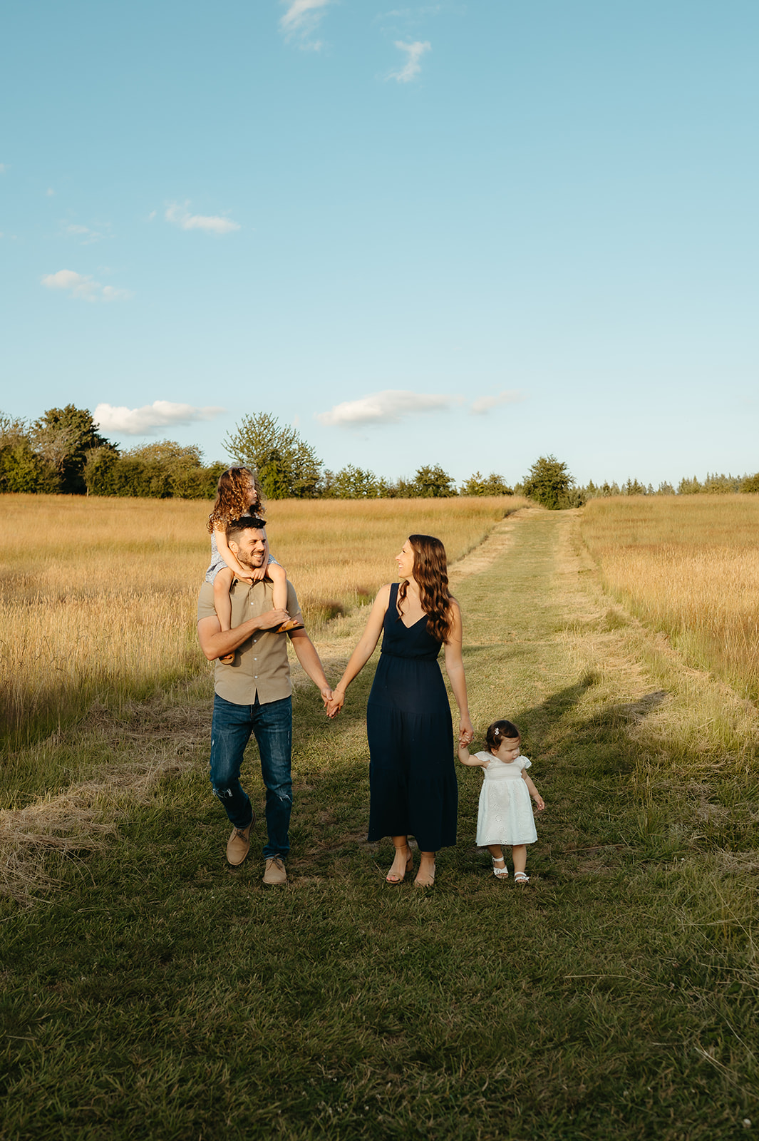 Parents walk down a grassy path with their children, surrounded by golden fields. A timeless and candid family photography session capturing movement and joy.