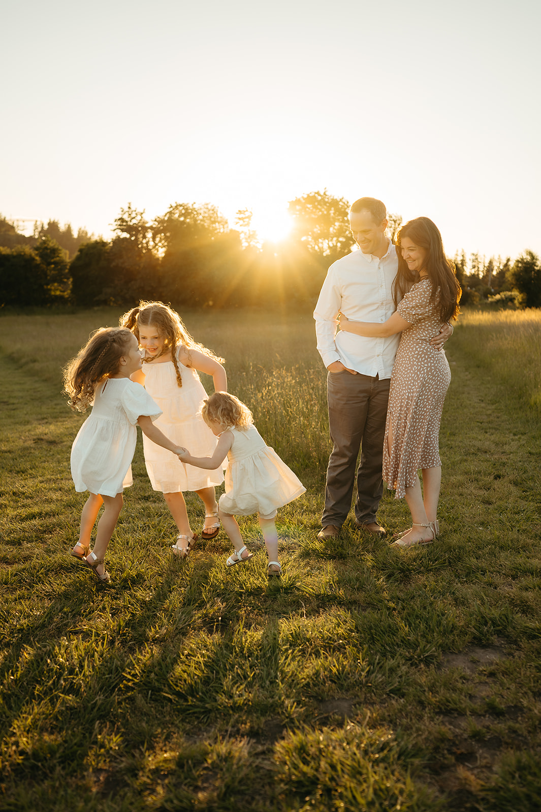 Mother and her three daughters in a sunlit field during a golden hour spring photography session. Soft, neutral dresses with warm tones for an effortlessly timeless family look.