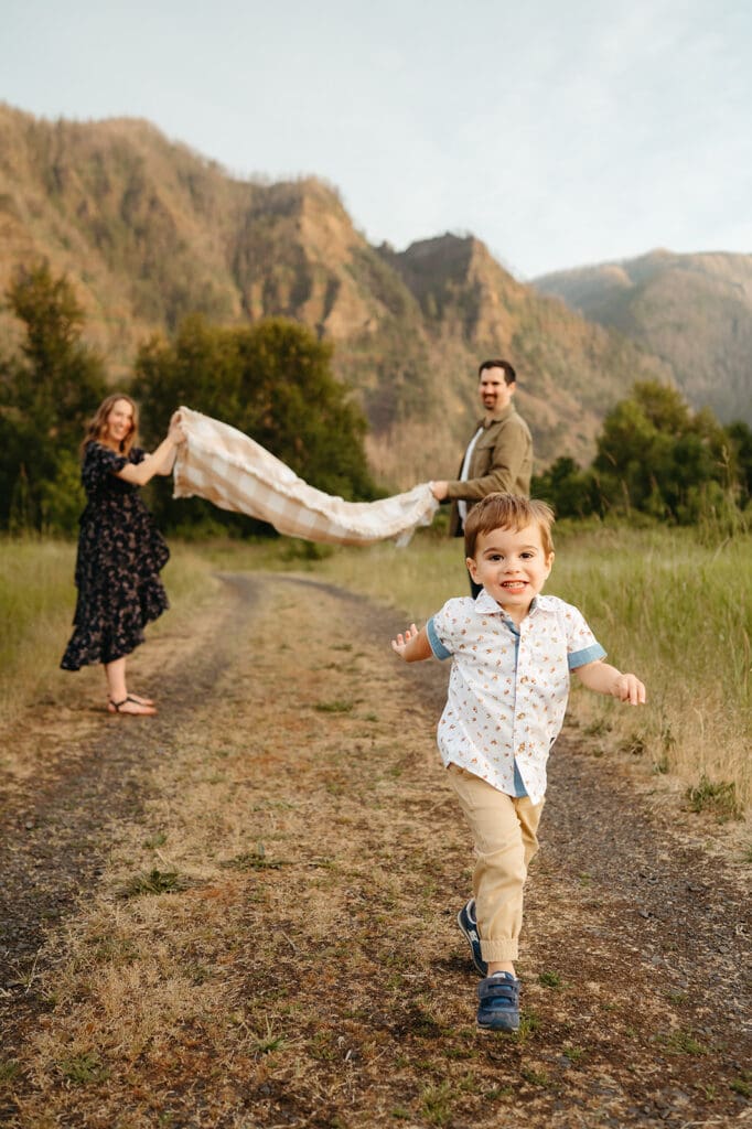 spring family photos in portland oregon featuring a little boy running through a blanket with the columbia river gorge in the backdrop