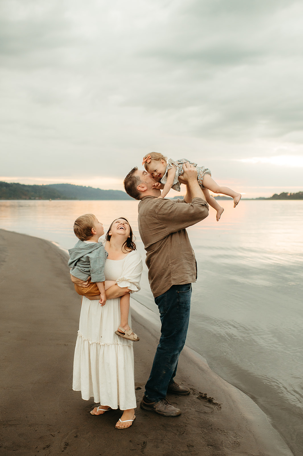 Family of four enjoying a playful moment by the water at sunset during a Portland family photography session. Parents and children dressed in soft neutrals for a relaxed, natural look.