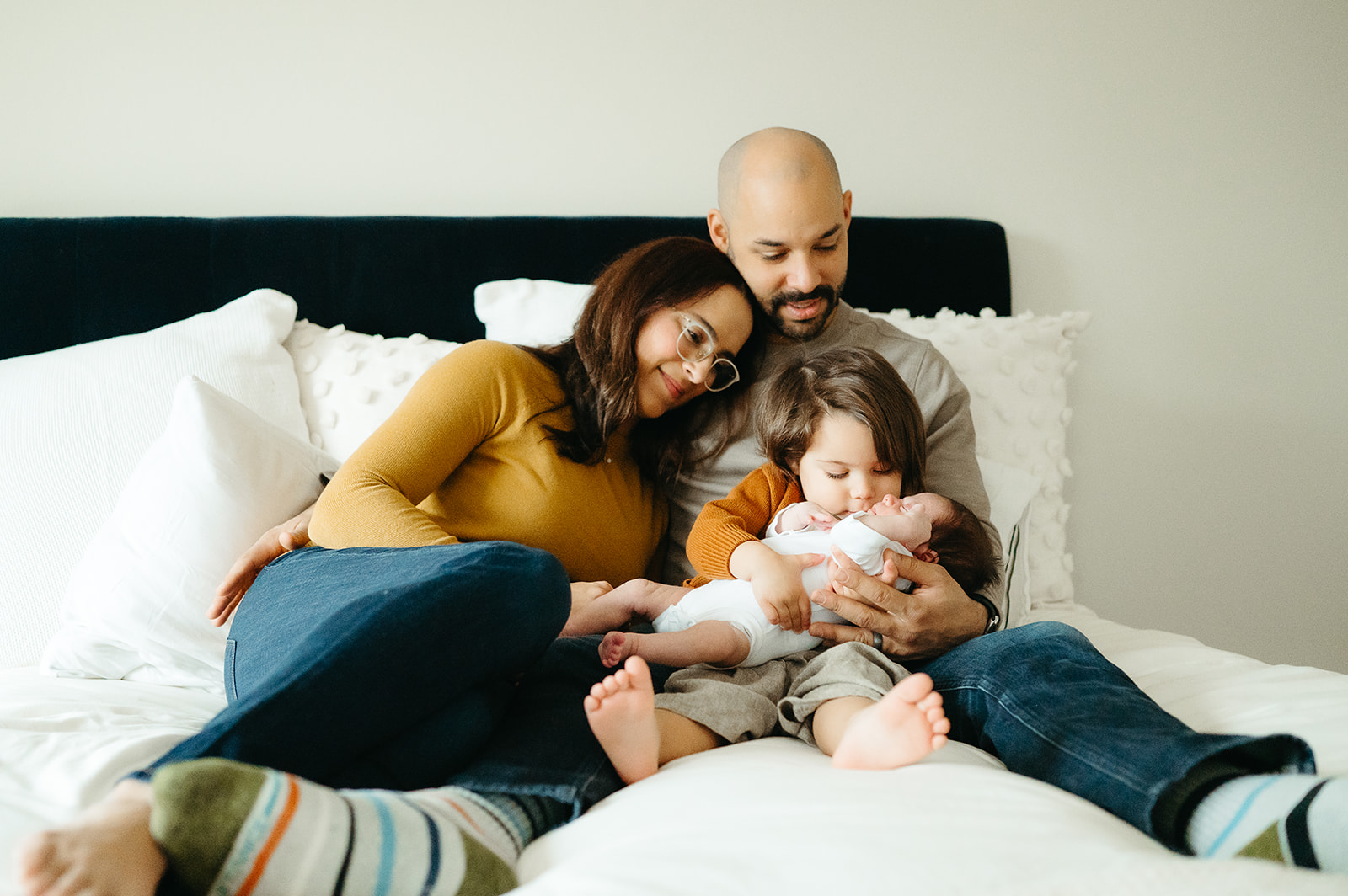 family cuddled up on a bed with toddler and newborn 