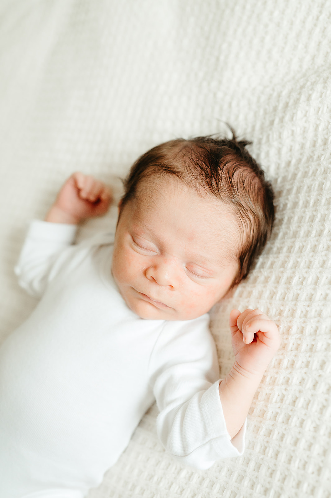 Newborn sleeping peacefully in white onesie during in-home Portland newborn session, photographed with natural light.
