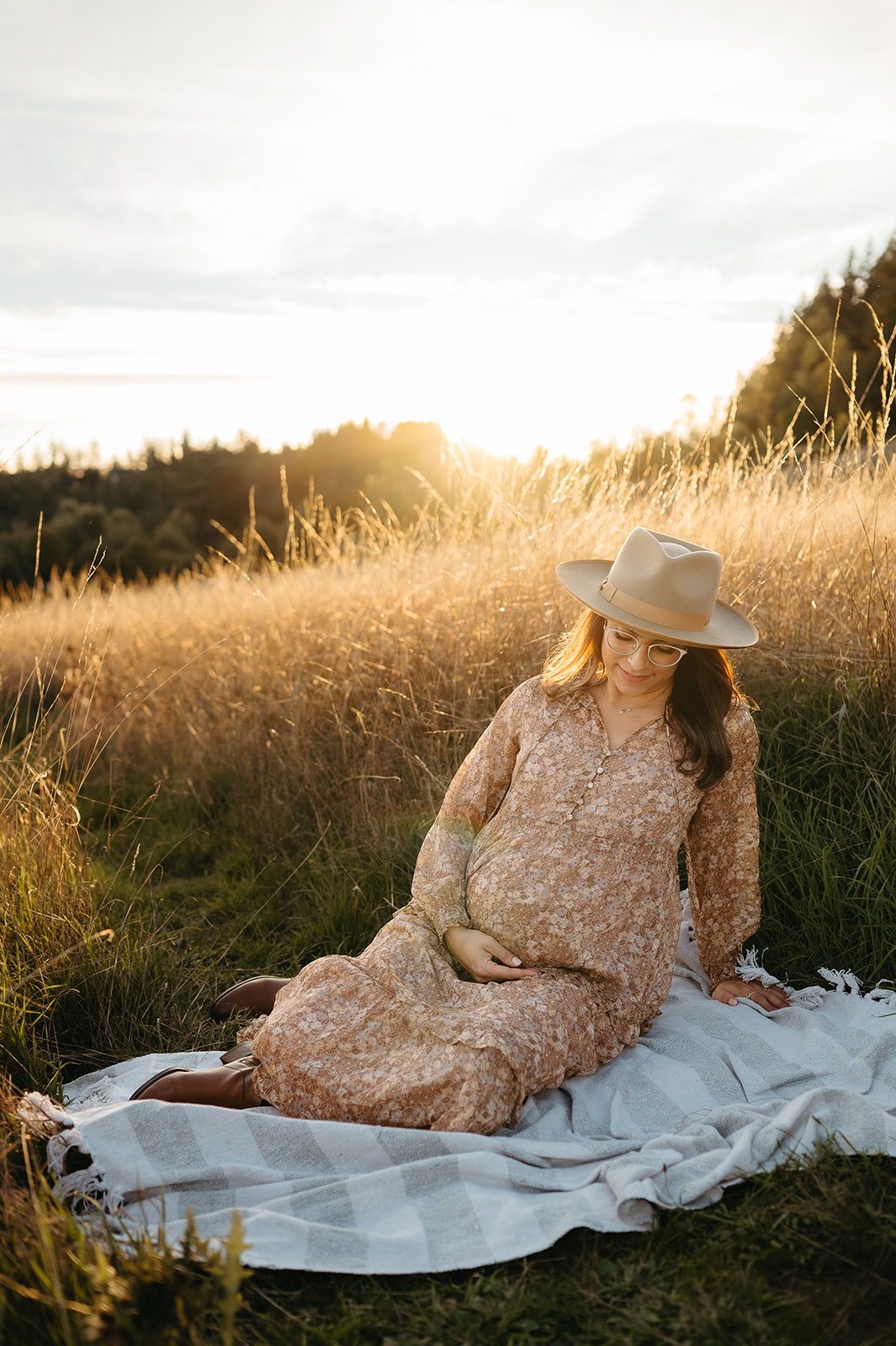 pregnant mother sitting in a field of golden grass looking down at her belly lovingly