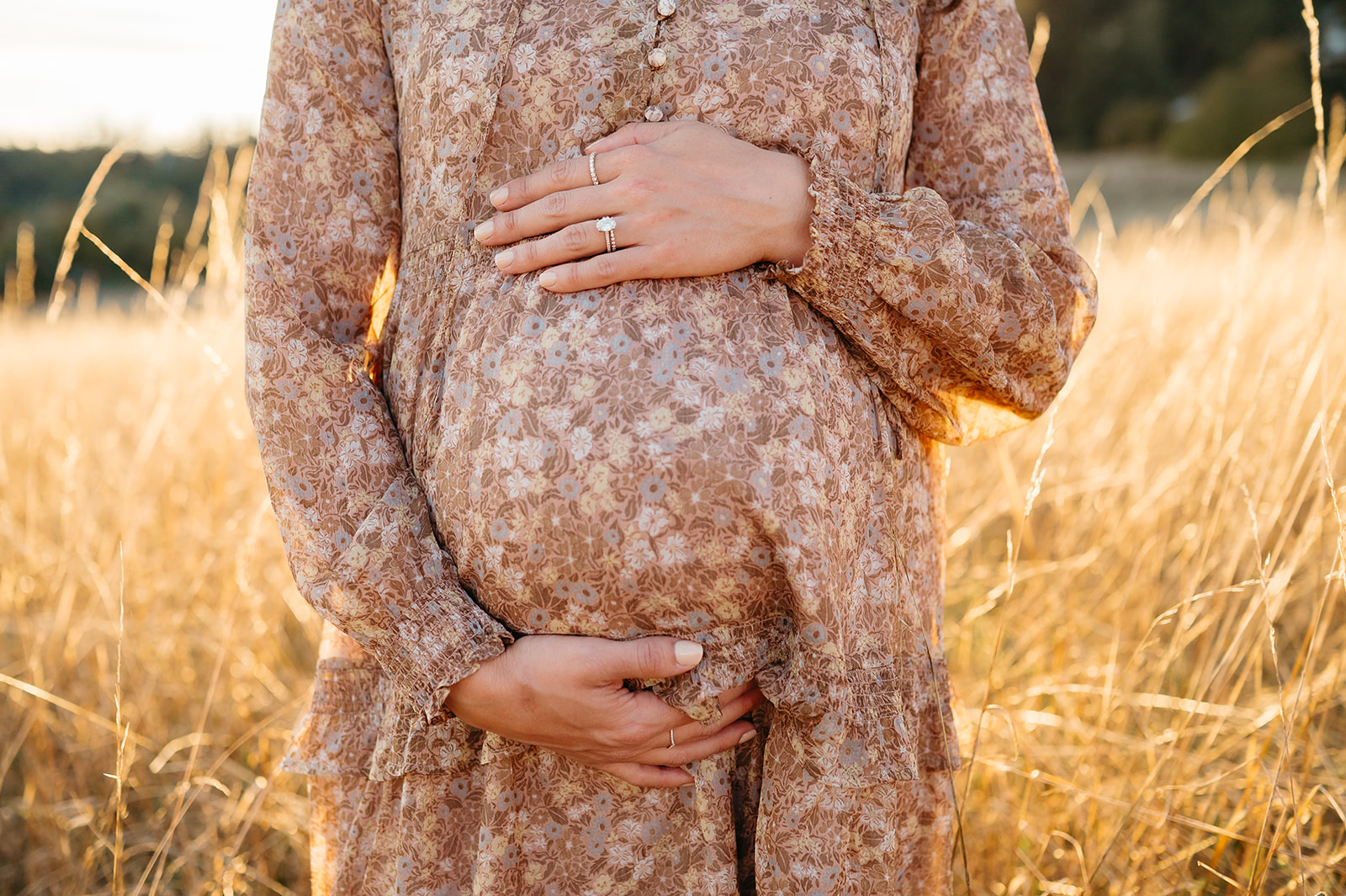 Close-up of pregnant belly with hands resting on floral dress during golden hour maternity session in Portland.